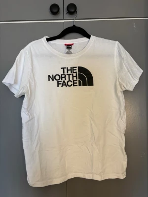Vit t-shirt från The North Face - Säljer en klassisk vit t-shirt från The North Face med svart logga tryckt på bröstet. T-shirten har rund halsringning och korta ärmar. Tillverkad i mjuk bomull som är skön att bära till vardags. Perfekt för dig som gillar enkel och stilren design. Är i xxl barn men är som S vuxen