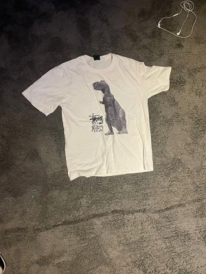 Vit t-shirt med dinosaurie - Vit t-shirt från med tryck av en dinosaurie och texten 'Big and Meaty' på framsidan. Klassisk passform med rund hals och korta ärmar. Perfekt för dig som gillar streetwear och coola prints.