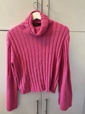 Rosa ribbstickad polotröja - Säljer en rosa ribbstickad polotröja med långa ärmar och lös passform. Tröjan har en hög polokrage och är tillverkad i ett mjukt stickat material. Perfekt för att hålla sig varm och snygg under kyliga dagar.