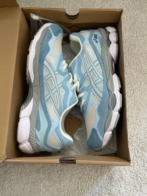 Ljusblå Asics - Snygga ASICS sneakers i ljusblått och vitt med grå detaljer. Ovandelen är i mesh och syntetmaterial för en fräsch och sportig look. Klassisk snörning och bekväm sula som passar perfekt till streetwear eller casual outfits.