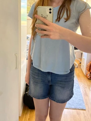Blå jeansshorts  - Säljer ett par blå jeansshorts med fem fickor och en hög midja. Shortsen har en enkel design utan synliga detaljer och är perfekta för sommaren. Jag köpte på MQ för flera år sedan och har bara använt 1 gång.