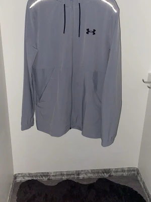 Grå vindjacka från Under Armour - Snygg grå vindjacka från Under Armour. Aldrig använts helt ny, köpt för 1200kr o säljer den för 849kr.