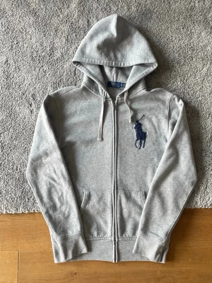 Grå hoodie från Polo Ralph Lauren - Grå Ralph Lauren zip hoodie i storlek XS säljes. I mycket bra skick och sparsamt använd. Klassisk zip hoodie med stor svart Ralph Lauren pony på bröstet.  ✅ Storlek XS ✅ Mycket bra skick ✅ Använd fåtal gånger ✅ Stor svart pony logga 🚚 Snabb frakt  Hör gärna av er vid frågor eller om ni vill ha fler bilder!