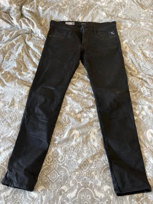 Svarta slim jeans från Replay - Snygga svarta slim fit jeans från Replay med klassisk femficksmodell och dragkedjegylf. Jeansen har diskreta Replay-detaljer på fickan och är tillverkade i ett stretchigt material för skön passform. Perfekta till alla typer av outfits.