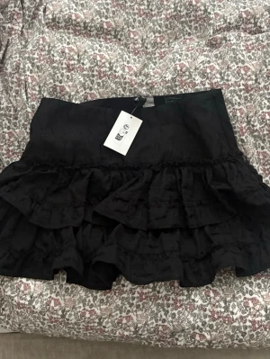 Svart volangkjol  - Supersnygg svart vilangkjol oanvänd med prislapp kvar från H&M i storlek 36.