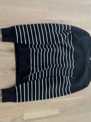 Randig stickad tröja från Uniqlo - Snygg svart stickad tröja från Uniqlo med vita horisontella ränder över hela plagget. Tröjan har rund halsringning och långa ärmar. Perfekt för dig som gillar klassisk och stilren design.
