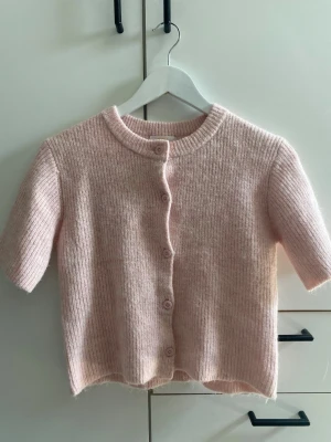 Ljusrosa kortärmad kofta - Söt ljusrosa kofta med korta ärmar och rund hals. Koftan har ribbstickad struktur och knäpps med matchande knappar framtill. Ifrån Gina Tricot Young i storlek 146/152. Jätte fint skick endast använd ett fåtal gånger! Tveka inte att höra av dig om du har några frågor🫶🏼