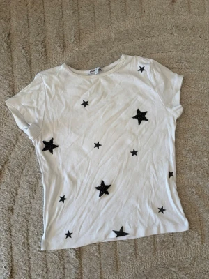 Vit t-shirt med svarta stjärnor - Cool T-shirt ifrån subdued. Den har detaljer med stjärnor där några utav dem är gjorde av små stenar. Mycket fin och passar att ha till skolan såval som en finare tillställning. 