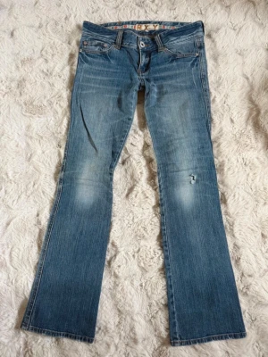 Blå bootcut jeans från Roxy - Snygga blå bootcut jeans från Roxy med slitningar och broderade detaljer på bakfickorna. Jeansen har låg midja, klassisk femficksmodell och är perfekta för en avslappnad och trendig look.