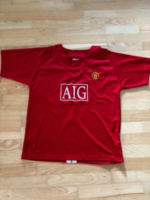Manchester United Tröja 07/08 med Tevez - Röd Manchester United matchtröja från säsongen 2007/2008. Tevez på ryggen med nummer 32. Tröjan är lite sliten och har ett hål men det syns och stör inte. Tröjan är XL i barnstorlek och XS/S i vuxenstorlek. Skriv om det är några frågor om tröjan! 
