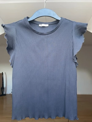 Ribbad topp - Supersöt ribbad topp från Zara i svart. Toppen har volangdetaljer vid ärmöppningarna och en rund halsringning. Skulle säga den även passar en  S