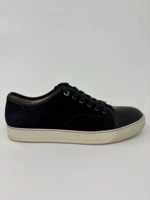 Mörkblå sneakers med lackad tå - Snygga mörkblå sneakers med ovandel i mocka och en glansig, svart lackad tå. Skorna har vita sulor och svarta skosnören. Metallfärgade öljetter ger en clean look. Perfekta för dig som vill ha en stilren men ändå unik sneaker.