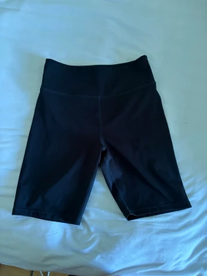 Svarta cykelshorts med hög midja - Säljer ett par svarta cykelshorts med hög midja. De är tillverkade i ett stretchigt och mjukt material som passar perfekt för träning eller vardagsaktiviteter. Shortsen har en enkel och stilren design utan synligt märke.