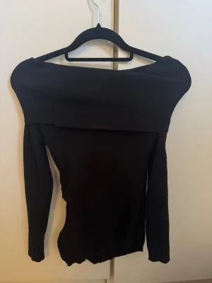 Svart offshoulder topp - Trendig svart offshoulder topp med lång ärm och bred kant över axlarna. Sitter tight och har en stilren, enkel design som passar perfekt till jeans eller kjol. Materialet känns mjukt och stretchigt, vilket gör den bekväm att bära.