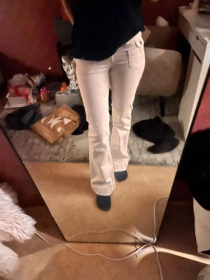 Vita bootcut jeans med låg midja - Säljer ett par vita bootcut jeans med låg midja med  fickor fram och bak. Jeansen har en snygg passform som sitter tajt över låren och släpper ut vid vaden. Perfekta för en trendig och avslappnad look. De är lite krämig vit 