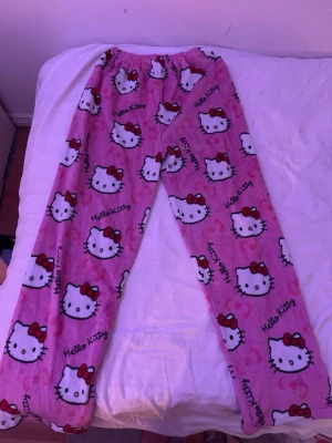 Hello Kitty rosa pyjamasbyxor XXL - Mysiga rosa pyjamasbyxor från Aslan med Hello Kitty-motiv över hela byxan. Tillverkade i 100% polyester för extra mjuk och skön känsla. Perfekta för chillkvällar hemma. Resår i midjan för bekväm passform. Det är ju olika passformer i Asian än i Europa så kolla upp det först innan ni köper! Så skulle säga på ett ungefär om man har M i storlek så ska man köpa XL eller XXL😊