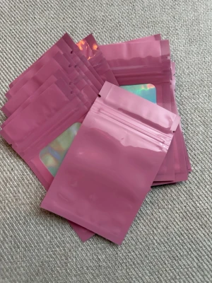 20st rosa zip-påsar, 10x6cm - Säljer ett gäng små zip-påsar i rosa plast med ett genomskinligt holografiskt fönster på framsidan. Perfekta för förvaring av småsaker, smycken eller andra prylar. Påsarna är återförslutningsbara och har en modern look. Storlek: 10x6cm 