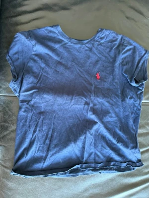 Marinblå t-shirt från Polo Ralph Lauren - Klassisk marinblå t-shirt från Polo Ralph Lauren med korta ärmar och rund hals. T-shirten har den ikoniska röda logotypen broderad på bröstet och är gjord i mjuk bomull för en skön känsla. Perfekt till jeans eller shorts.