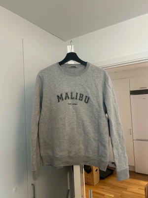 Grå sweatshirt från Saint Laurent - Säljer en grå sweatshirt från Saint Laurent med  'Malibu' tryck på bröstet. Använd fåtal ggr så i fint skick. Storlek M men liten i storlek så passar en S snarare. Pris kan diskuteras 
