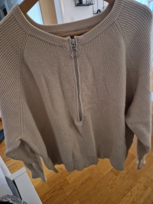 Beige stickad tröja Carin Wester - Beige stickad tröja från Carin Wester i storlek S. Tröjan har en ribbad struktur, lång ärm och en snygg half zip-dragkedja framtill med rund ringdetalj. Perfekt för lager-på-lager och chill stil.