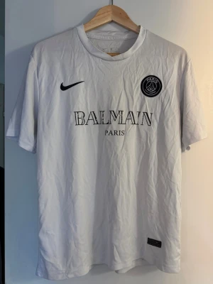 Paris Balmain tshirt  - Paris Balmain tshirt i träningsmaterial som är köpt hos Miinto 🌟 Lite slitning på trycket (se bild 2) men inget som syns på avstånd samt inget man tänker på enligt mig