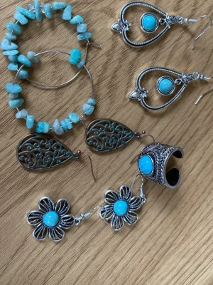Set med turkosa örhängen i bohostil - Säljer ett set med tre par örhängen i boho-stil. Ett par stora ringar med turkosa pärlor, ett par droppformade örhängen i silverfärgad metall med turkos sten, samt ett par blommiga örhängen med turkos detalj. Perfekt för dig som gillar unika accessoarer och färgglada detaljer.