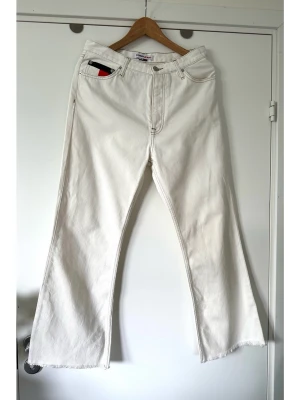 Tommy Hilfiger - vita jeans - storlek M (W30 L32) - Stilrena vita jeans från Tommy Hilfiger / Tommy Jeans i populära modellen Harper High Rise Flare, i storlek W30 L32 (motsvarande M). Tidlös modell med hög midja och lätt utsvängda ben med råa kanter. Detaljer inkluderar en liten flagglogga på myntfickan fram och en större logga baktill i midjan. Gylfen stängs med dragkedja och knapp. Stabil vit denim i 100% bomull, så bra material som andas. En välgjord tidlös klassiker som kommer hålla säsong efter säsong. Nypris 1499:-. Mycket gott skick!