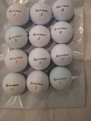 TaylorMade golfbollar mixade modeller - Säljer ett set med 12 vita golfbollar från TaylorMade i olika modeller som RBZ Soft, Tour Preferred X, Burner Soft och Rocketballz. Bollarna har olika siffror och tryck, tillverkade i slitstarkt material och passar perfekt för golfentusiasten som vill ha variation på banan.