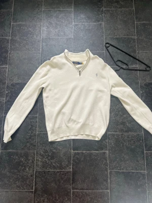 Ralph Lauren Tröja - Halv Zip - Medium - Klassisk creame vit  långärmad tröja från Polo Ralph Lauren med halvzip och broderad logga på bröstet. Tröjan har ribbade muddar och är tillverkad i ett mjukt material som känns skönt mot huden. Perfekt för en stilren och avslappnad look.