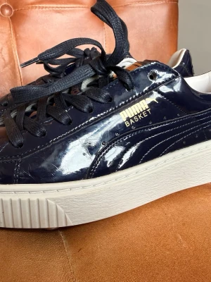 Puma Basket sneakers navy - Snygga Puma Basket sneakers i mörkblått lack med vita, tjocka sulor och svarta skosnören. Guldiga detaljer vid loggan på sidan. Klassisk låg modell med modern touch och glansig finish som sticker ut. Se bilderna för skicken.