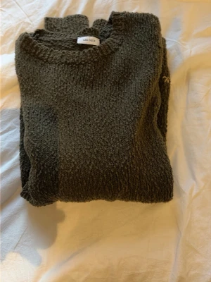 Mörkgrön stickad tröja Les Deux - Mysig mörkgrön stickad tröja från Les Deux med rund halsringning och långa ärmar. Tröjan har en diskret broderad logga vid nederkanten och är tillverkad i ett grovstickat material som ger en avslappnad look. Är i storlek 170 men är som S