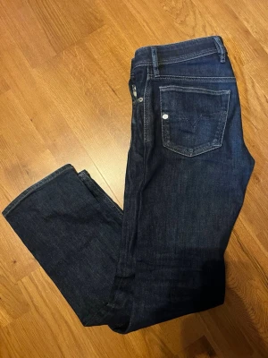 Mörkblå jeans från Diesel - Snygga mörkblå jeans från Diesel med klassisk femficksdesign och raka ben. Jeansen har tydliga kontrastsömmar och en ikonisk bakficka med V-formad söm. Perfekta för en stilren och avslappnad look. Storleken är W30, L30. Hör av er om ni har några frågor!