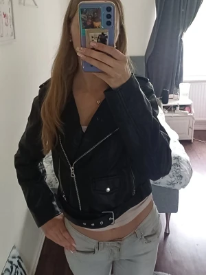Svart skinnjacka -  svart skinnjacka i klassisk bikerstil med silvriga dragkedjor, fickor och bälte i midjan.  Perfekt för dig som vill ha en tidlös och trendig jacka till din garderob. Det står att wwt är storlek L men skulle säga mer M/S