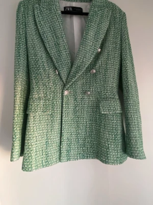 Grön tweedkavaj från Zara - Stilren grön tweedkavaj från Zara med dubbelknäppning och silvriga knappar. Kavajen har breda slag, två fickor med lock framtill och en kroppsföljande look. Materialet är strukturerat.Aldrig använd och prislappen sitter kvar❣️