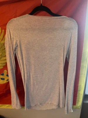 Ljusgrå långärmad topp - En basic ljusgrå långärmad topp i mjukt och stretchigt material. Enkel och stilren design med rund halsringning och smal passform. Perfekt att matcha med jeans eller kjol för en avslappnad look.