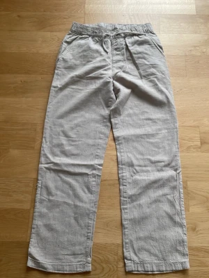 Ljusgrå linnebyxor raka ben - Säljer ett par ljusgrå linnebyxor med raka ben och avslappnad passform. Byxorna har klassisk midja och sidfickor. Perfekta för en chill och stilren look. Materialet är svalt linne som ger en skön känsla.