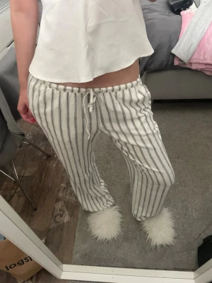 Randiga linnebyxor med dragsko - Säljer ett par vita linnebyxor med svarta vertikala ränder och dragsko i midjan. Byxorna har en avslappnad och rak passform, perfekta för chill dagar. Materialet ser ut att vara lätt och luftigt, vilket gör dem sköna att bära.