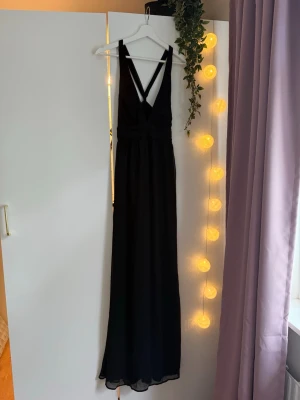 Svart långklänning - Svart långklänning med djup v-ringning från Nelly, har axelband som korsas i ryggen. Köpt second hand, är superfin men för stor för mig! Perfekt till bal eller andra formella tillfällen 💞🥂