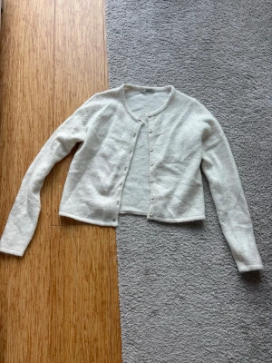 Vit kofta från Gina Tricot - Söt vit kofta från Gina Tricot med rund halsringning och knappar framtill. Koftan är i ett mjukt, fluffigt material och har långa ärmar. Enkel och stilren modell som passar perfekt till jeans eller kjol. Storlek M men passar S-XS
