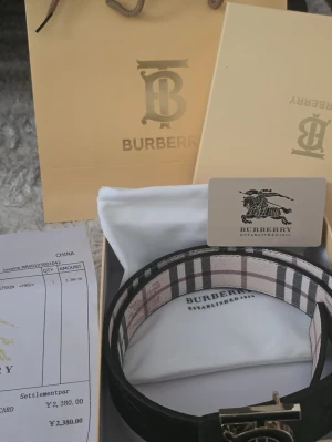 Burberry bälte - Stilrent svart bälte från Burberry med klassiskt rutigt mönster och präglad logga. Snyggt metallspänne med Burberrys ikoniska 'B'. Perfekt accessoar för att lyfta din outfit.