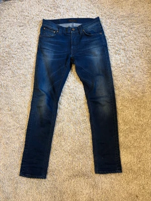 Mörkblå slim fit jeans från Nudie jeans - Snygga mörkblå slim fit jeans från Nudie med klassisk femficksdesign. Jeansen har normal midja och är tillverkade i denim för en bekväm slim fit passform.                                                             Modell: Lean Dean.                                                               Läng 32/100cm.                                                                   Midja: 29/38cm