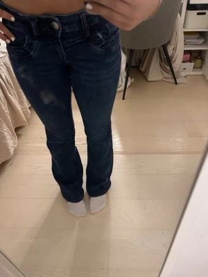 Mörkblå bootcut jeans med fickdetaljer - Snygga mörkblå bootcut jeans med markerade fickor och lätt slitning framtill. Jeansen har låg midja och klassisk femficksdesign. Perfekta för dig som gillar en tidlös och trendig look.
