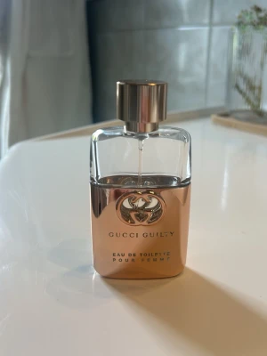 Gucci Guilty Pour Femme Eau de Toilette - Gucci Guilty Pour Femme Eau de Toilette med elegant flaska i guld och transparent glas. Flaskan har en lyxig metallkork och ikonisk Gucci-logga framtill. Perfekt för dig som gillar exklusiva dofter och snygg design på parfymhyllan. Mer än hälften kvar.