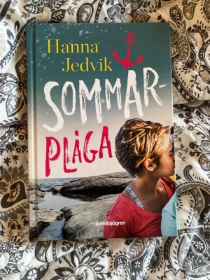 Sommarplåga av Hanna Jedvik - En ungdomsroman med hård pärm, färgstarkt omslag och illustration av en person vid havet. Titeln 'Sommarplåga' är tryckt i vitt och rosa, och boken har en tydlig sommarkänsla. Perfekt för dig som gillar samtida skönlitteratur med tonårstema.