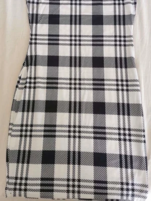 Svartvit rutig kort klänning - Snygg svartvit kort klänning med klassiskt rutigt mönster. Figurnära passform och ärmlös design, perfekt för dig som gillar en stilren och trendig look. Tillverkad i mjukt material som känns bekvämt mot huden.