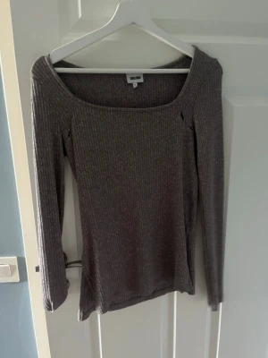 Ribbad grå långärmad topp H&M - Ribbad långärmad topp från H&M i en snygg grå nyans. Toppen har en bred, fyrkantig ringning och är figurnära i modellen. Perfekt att styla med jeans eller kjol för en enkel och trendig look.