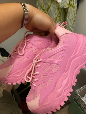 Chunky rosa sneakers  - Säljer ett par chunky sneakers f i helrosa färg. Skorna har grov sula, mesh- och syntetdetaljer samt klassisk snörning. Perfekta för dig som vill sticka ut med en färgstark look och gillar streetstyle.