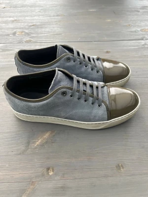 Lanvin - Ett par snygga Lanvin Cap Toe sneakers i gråblå mocka med olivgröna lackdetaljer på tån och runt snörningen. Skorna har gråblå skosnören och vit sula. Skorna är i storlek 43 och mycket bra skick nästan helt utan defekter då de knappt är använda av mig. Priset kan diskuteras, bara att höra av sig vid frågor💯