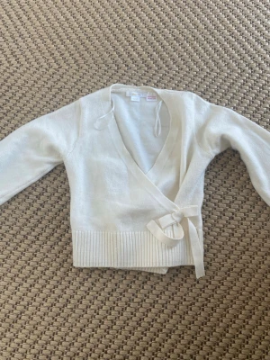 Vit omlottkofta med knytband - Snygg vit omlottkofta med knytband i midjan och bred ribbad mudd nedtill. Koftan har lång ärm och djup v-ringning, perfekt att styla med jeans eller kjol. Mjuk och skön stickad känsla.❤️💞