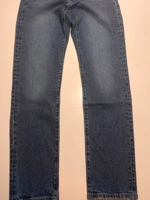 Klassiska raka blå Levis jeans - Ett par klassiska blå jeans med rak passform och normal midja. Jeansen har en tidlös tvätt och är tillverkade i denim, perfekt för en avslappnad stil. 